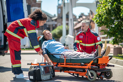 Serious ambulance physician securing the blood pressure cuff on the patient arm in the presence of her colleague